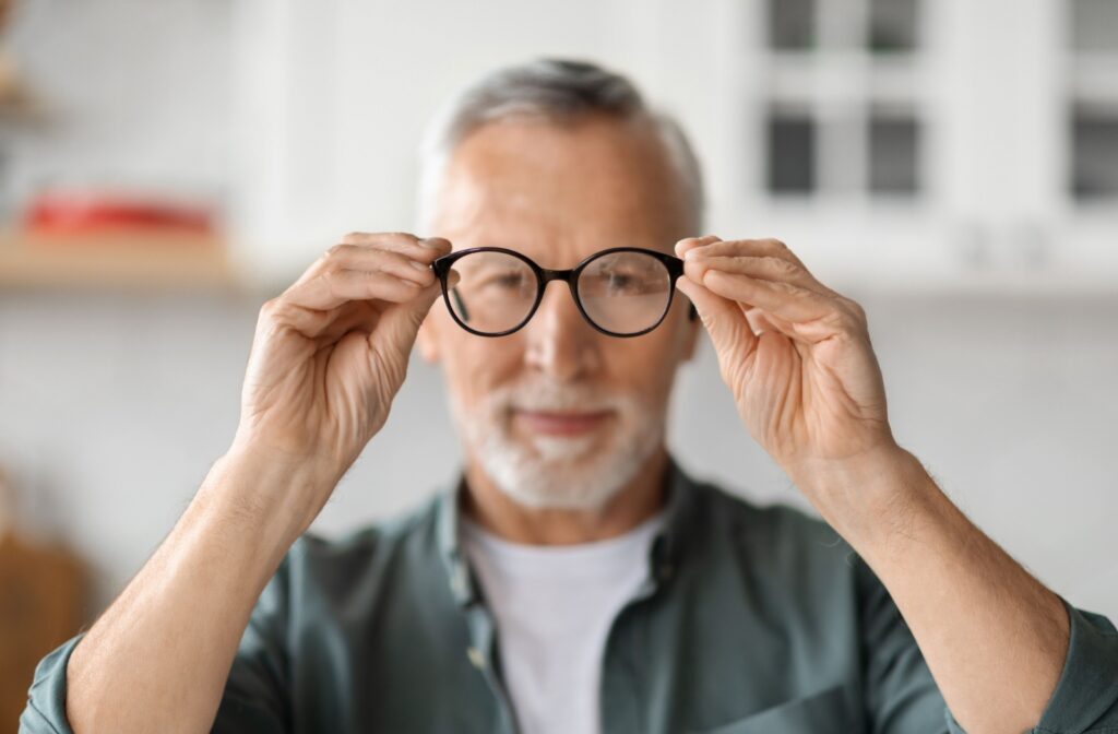 An adult with cataracts holding out a pair of glasses in front of their face.