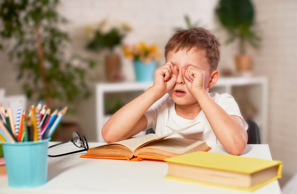 A child rubbing their eyes while doing school work.